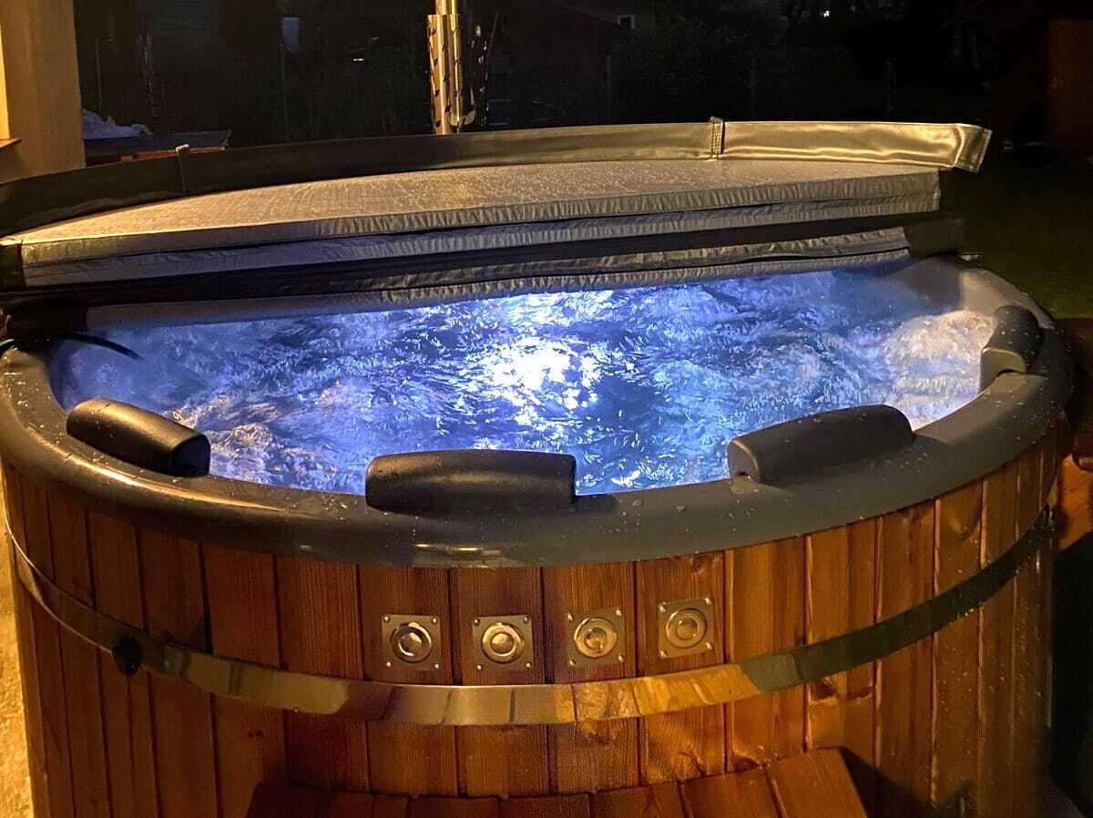 Una bañera de hidromasaje de madera con tapa de vidrio, visibles chorros de agua y estructura metálica.