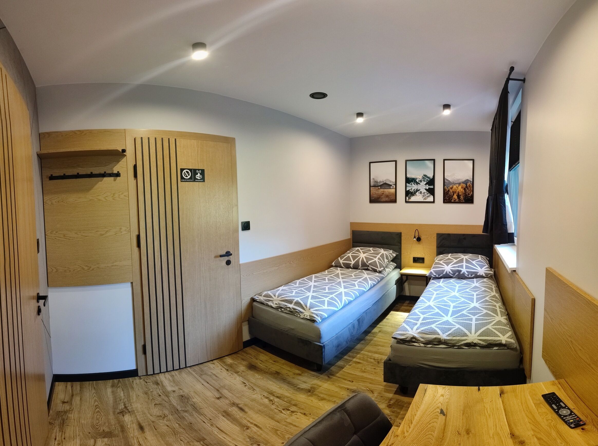 Una habitación de hotel compacta con dos camas individuales, un armario de madera, una mesita pequeña y un televisor.