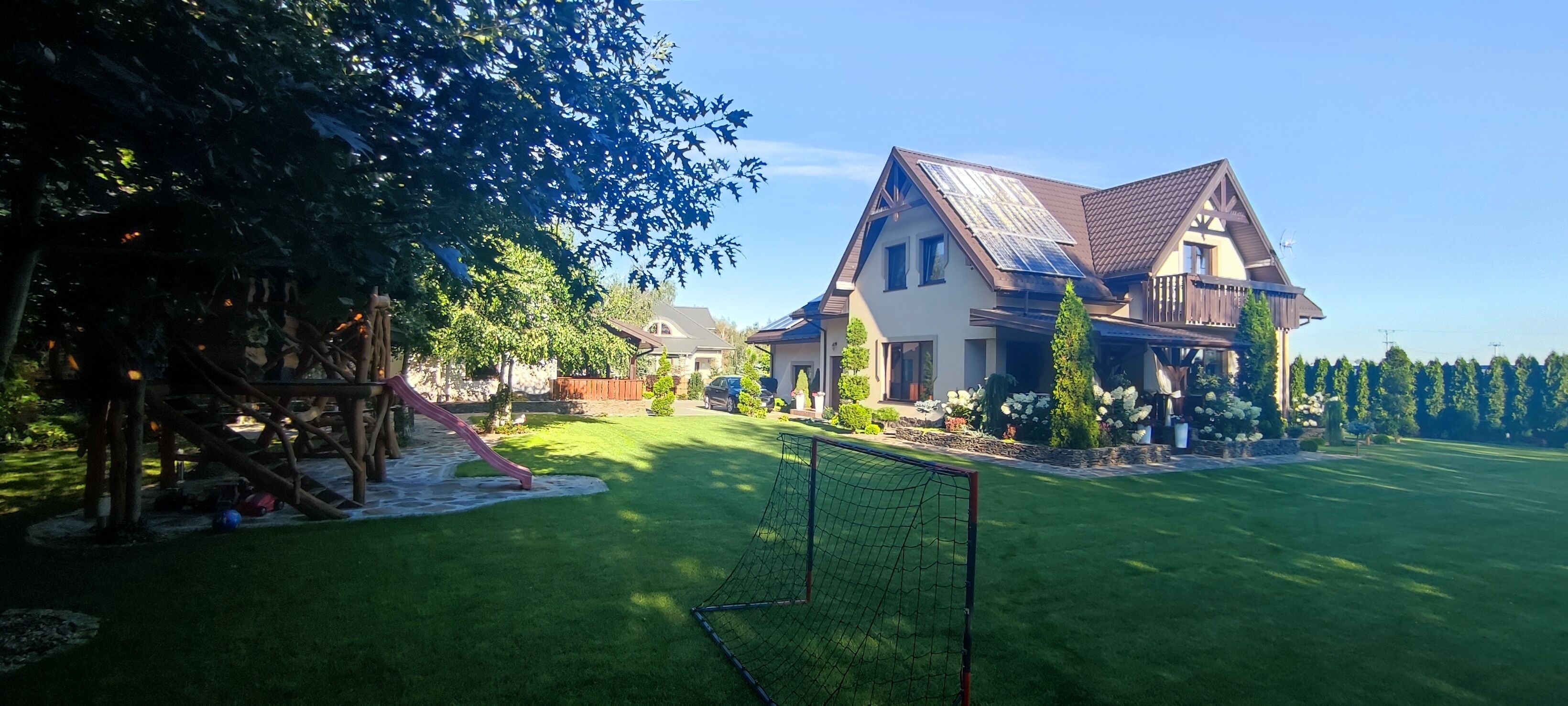 A residential property with a well-maintained lawn, a play area with a slide, and a large house with solar panels.