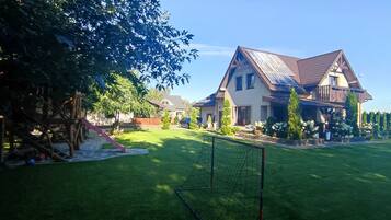 A residential property with a well-maintained lawn, a play area with a slide, and a large house with solar panels.