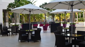 Un'area patio all'aperto con tavoli, sedie, ombrelloni e piante in vaso.