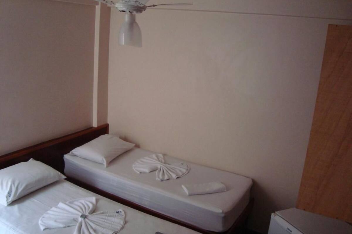 A hotel room with two beds, each with a neatly folded towel and a remote control on the bed. A ceiling fan is visible above the beds.