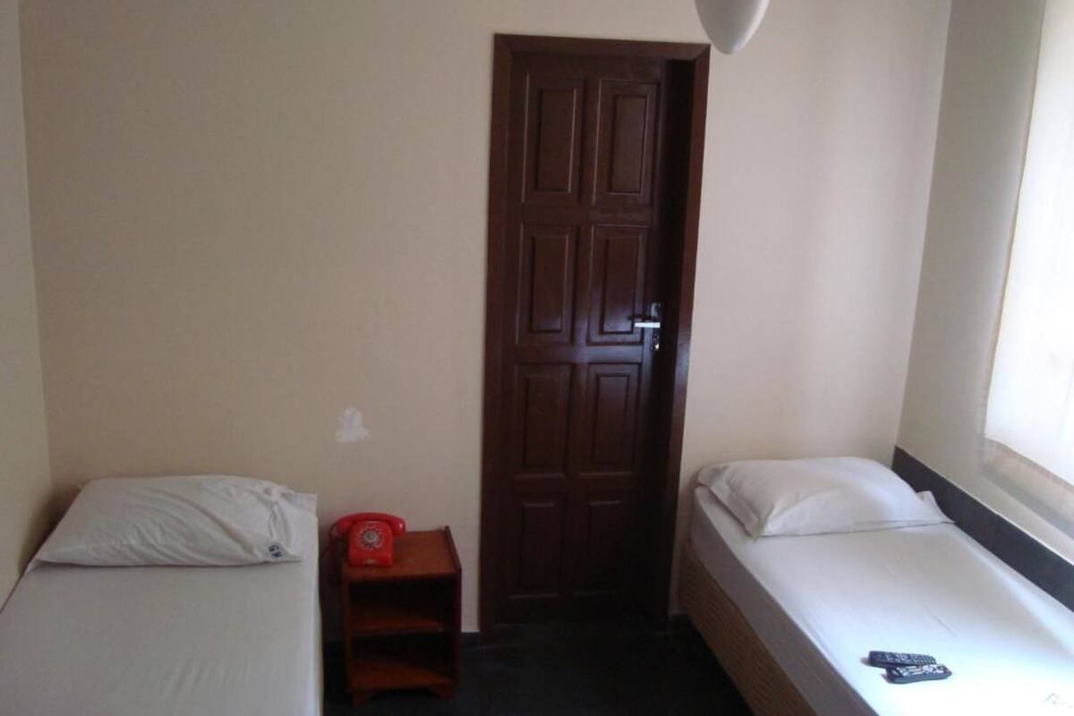 A small, simple room with two beds, a wooden door, and a small table with a red telephone.