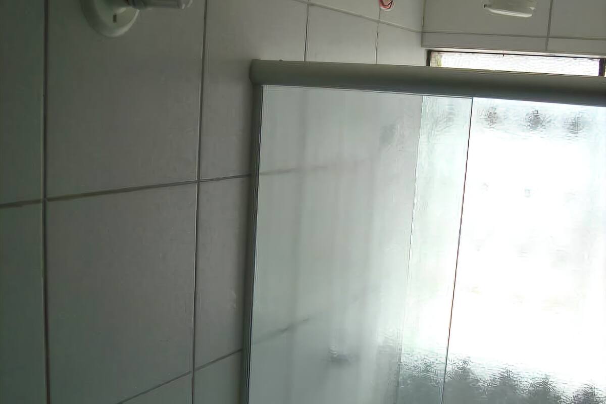 A bathroom with white tiled walls, a toilet, a shower enclosure, and a window.