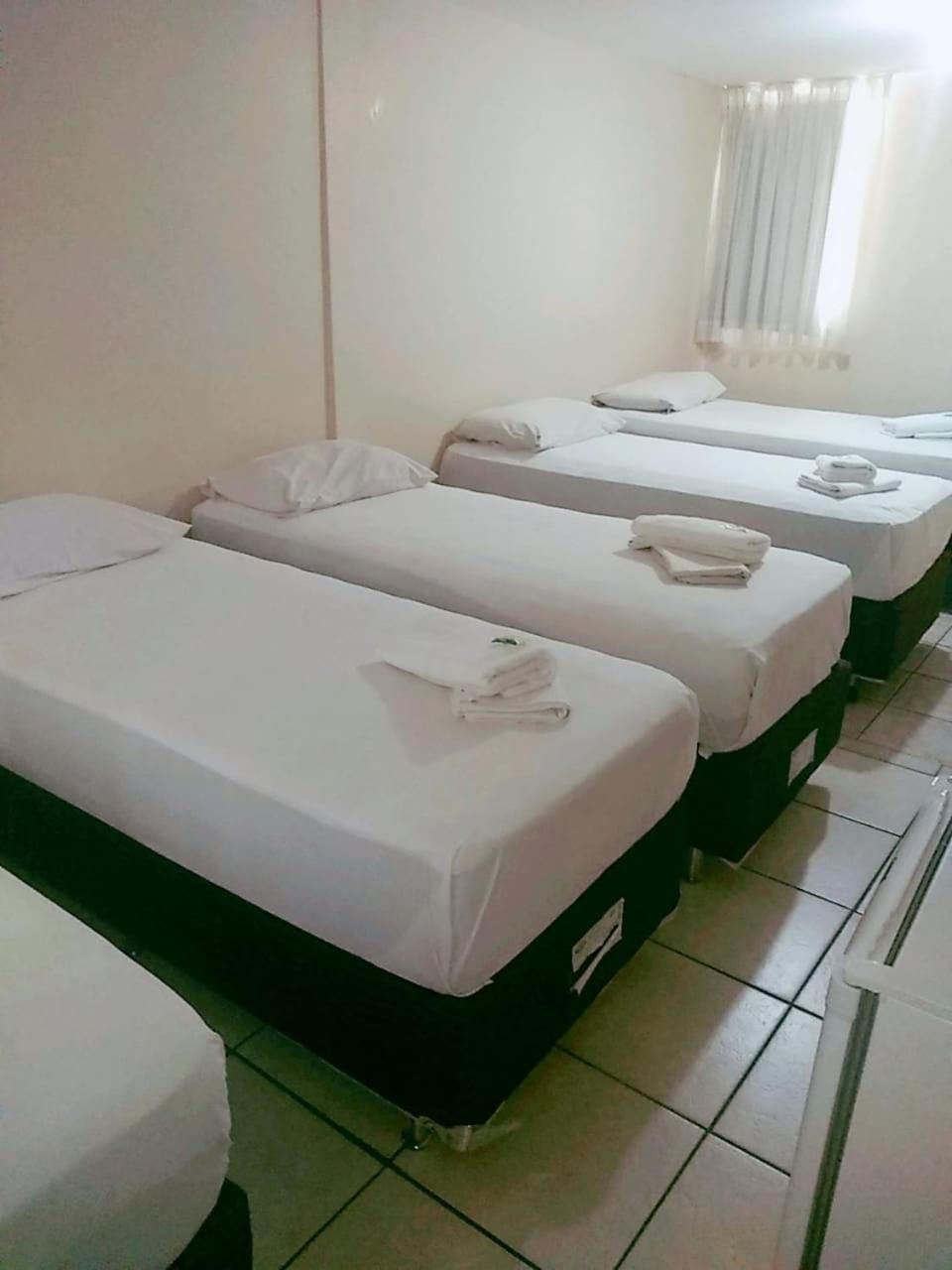 Quarto de hotel com três camas de solteiro, cada uma com colchão e travesseiro brancos, e cabeceira verde.