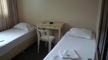 Quarto de hotel com duas camas de solteiro, uma escrivaninha e uma cadeira.