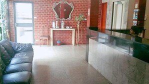 A lobby with a black leather sofa, a reception desk, a mirror, and a potted plant. - Goias Hotel (Goiania)