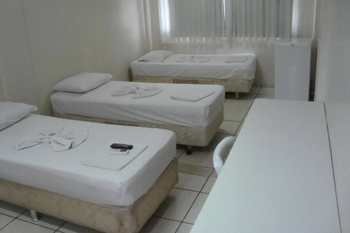 A hotel room with two beds, a small table, and a window with curtains.