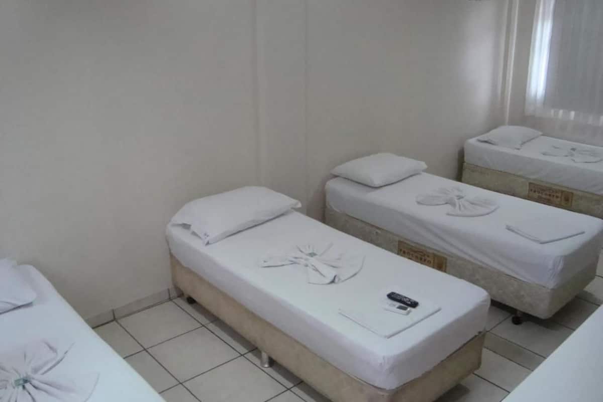 A room with three single beds, each with a pillow and a blanket. There is a small table with a remote control on it.