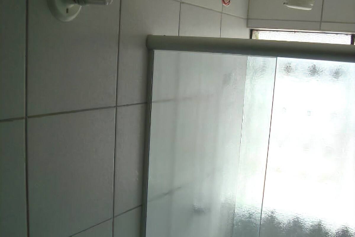 A bathroom with white tiled walls, a toilet, a shower curtain, and a ceiling fan.