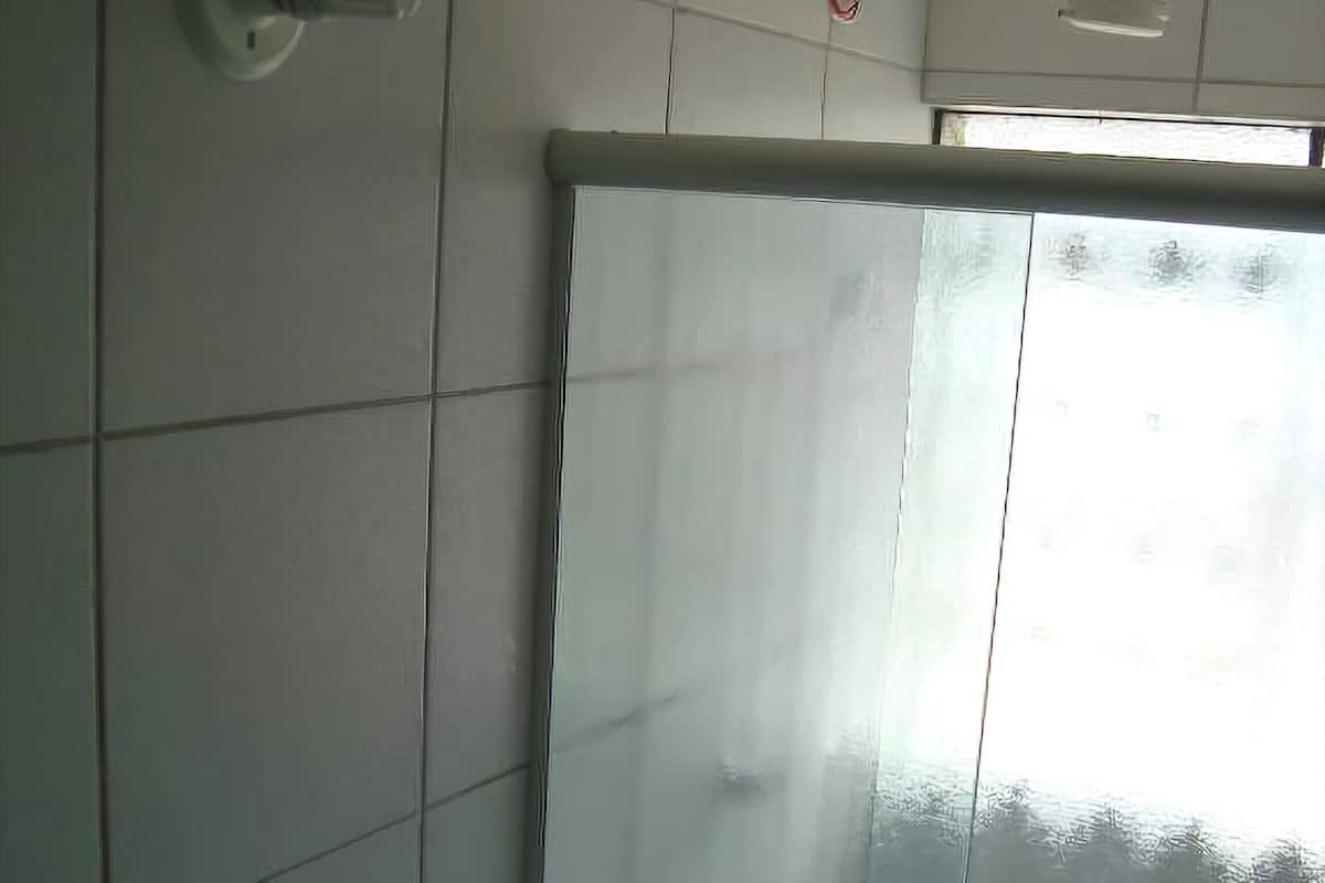 A bathroom with white tiled walls, a toilet, a shower curtain, and a ceiling fan.