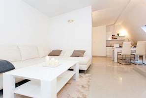 A modern living room with a white sofa, a coffee table, and a dining area with white chairs. - Studio Apartament Centrum Katowice (Katowice)