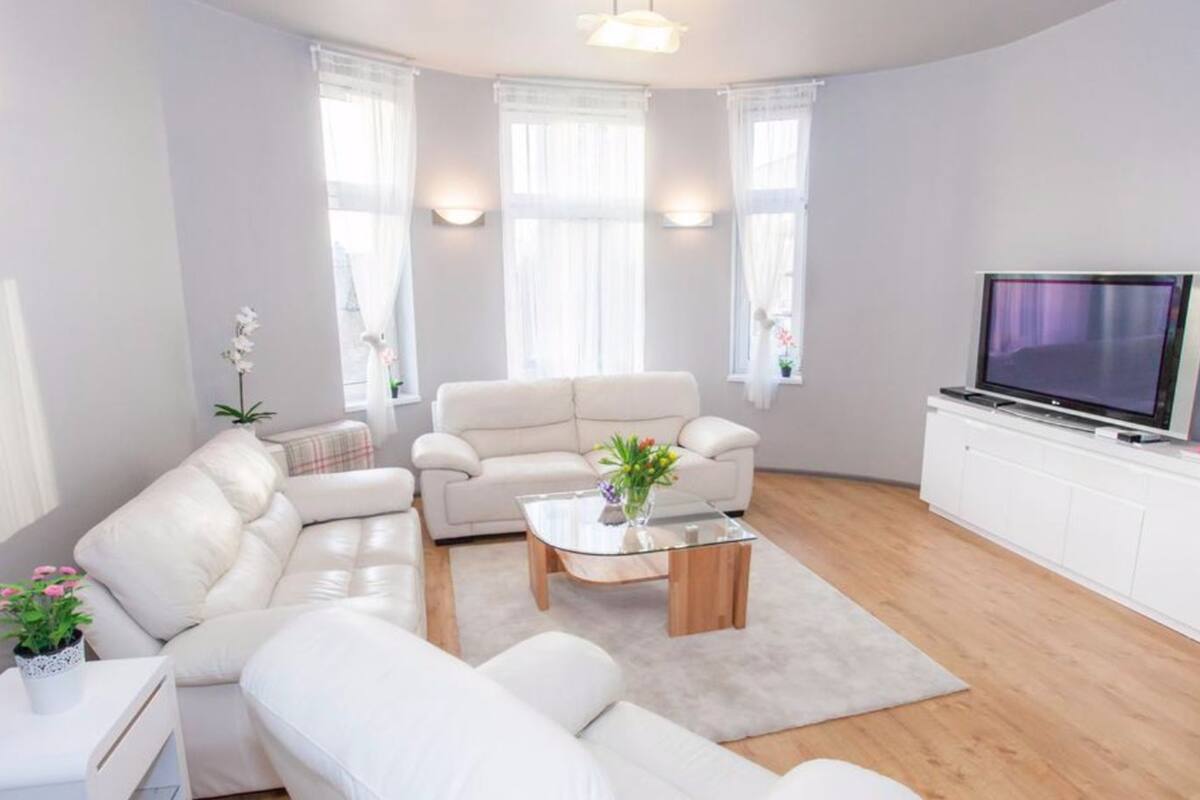 A modern living room with a white sofa set, a glass coffee table, and a flat-screen TV on a white cabinet.