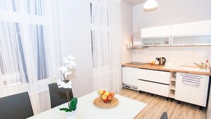 A modern kitchen with white cabinets, a wooden countertop, and a dining area with a white table and chairs. - Studio Apartament Centrum Katowice (Katowice)