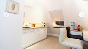 A modern kitchen with white cabinets, a sink, and a dining area with a chair and table. - Studio Apartament Centrum Katowice (Katowice)