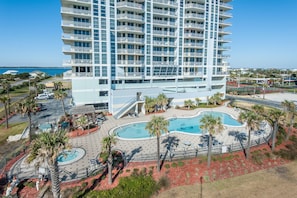 A high-rise hotel with multiple balconies, a swimming pool area with palm trees, and a view of the ocean. - Emerald Dolphin unit 1220 - Two Bedroom Condo (Pensacola Beach)