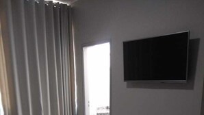 A hotel room with a bed, a flat-screen TV mounted on the wall, a window with curtains, and a view of the outside balcony. - Presidente Hotel - Passos (Passos)