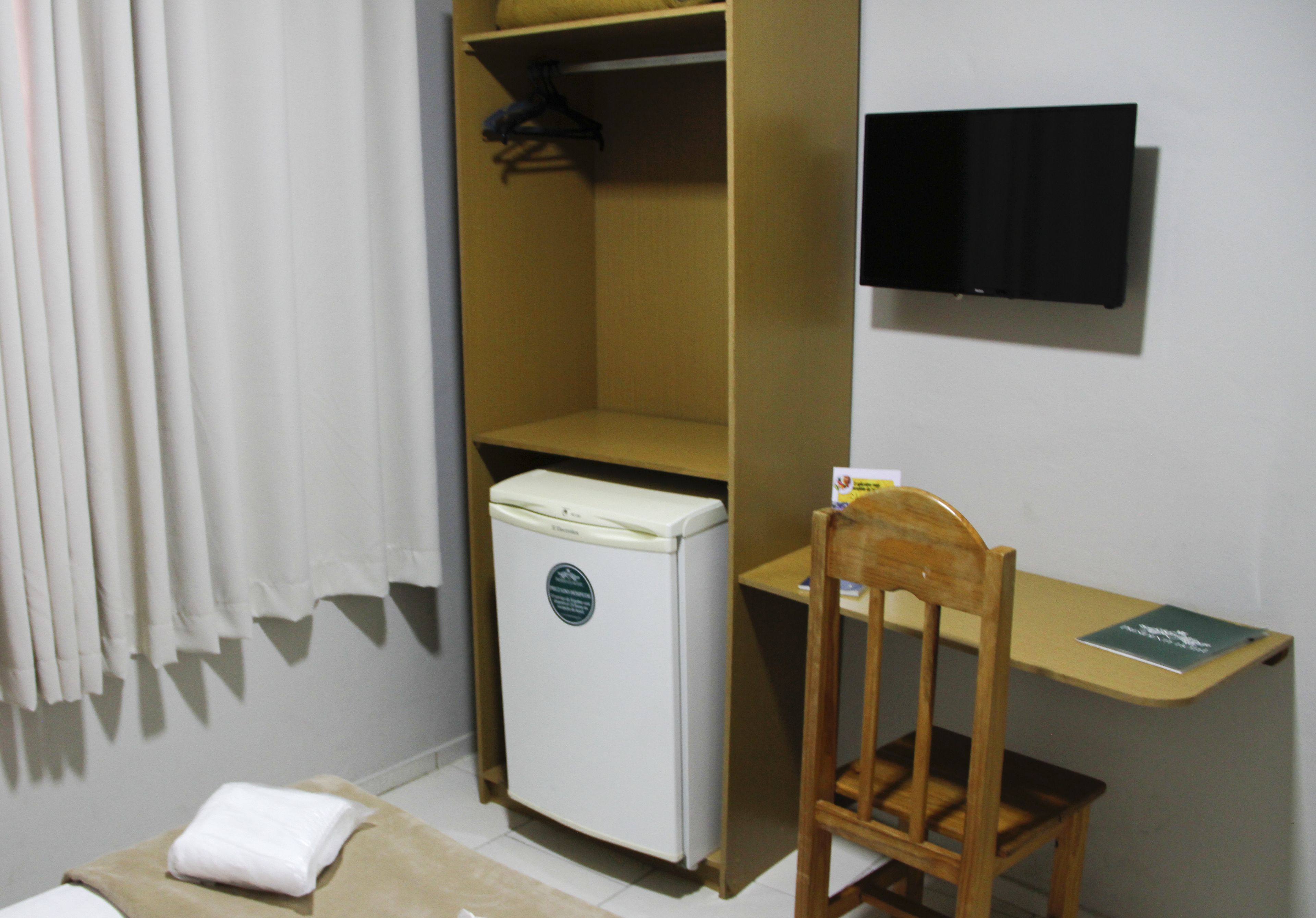 A compact room with a bed, a small desk, a chair, a wardrobe, and a refrigerator.
