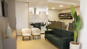A modern living room with a green sofa, two armchairs, a glass coffee table, and a potted plant. - Presidente Hotel - Passos (Passos)