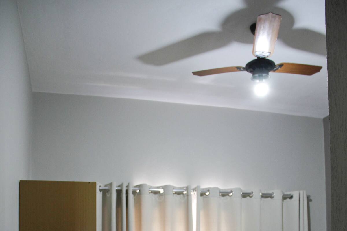 Una habitación de hotel con cama, escritorio, silla, ventilador de techo y televisor montado en la pared.