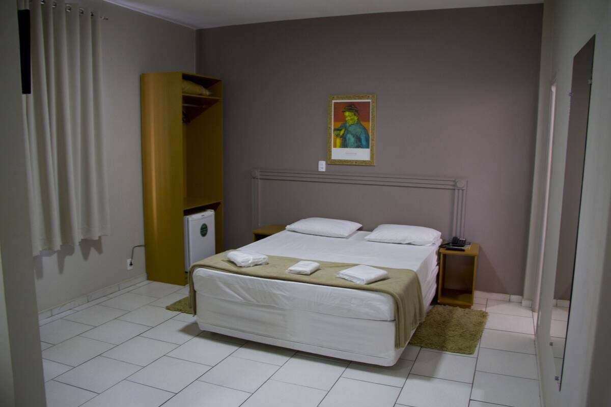 Una habitación de hotel con cama, mesita de noche, armario y un cuadro en la pared.