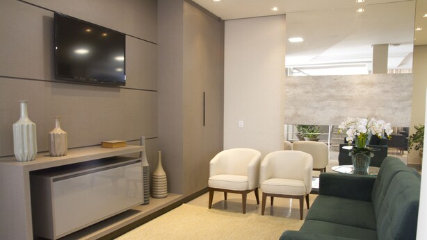 A modern living room with a flat-screen TV mounted on the wall, a grey sofa, two white armchairs, a coffee table, and decorative vases. - Presidente Hotel - Passos (Passos)