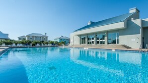 Une piscine à l’eau d’un bleu cristallin, entourée de chaises longues et bordée d’un bâtiment aux grandes fenêtres.