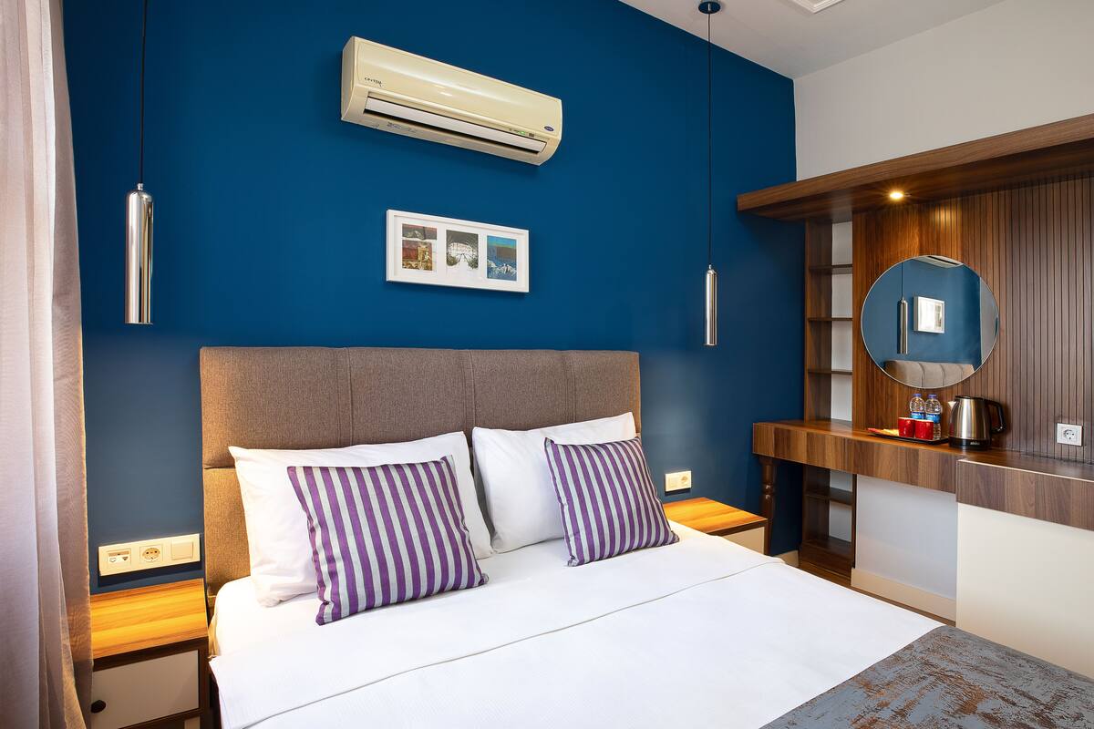 Une chambre d’hôtel moderne avec un grand lit, une tête de lit en bois, une table de chevet avec un miroir et un appareil de climatisation.
