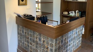 A reception desk with a patterned tile backsplash, a framed picture above, and a wooden bookshelf with books and a framed certificate. - Mono Hotel (Antalya)
