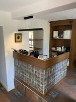 Un mostrador de recepción con un reverso de azulejos estampados, un cuadro enmarcado encima y una estantería de madera con libros y un certificado enmarcado.