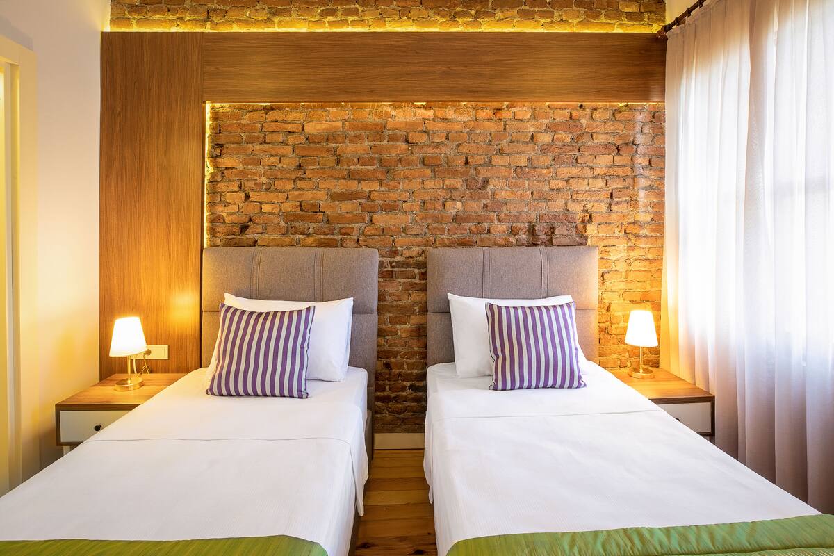 Une chambre d’hôtel avec deux lits, des têtes de lit en bois, un mur en briques et un plafond en bois.