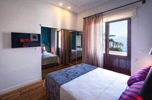Habitación de hotel con cama, televisor montado en la pared, ventana con cortinas y vistas al exterior.