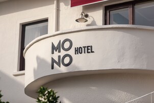 Un letrero de hotel con el nombre "MONO HOTEL" sobre una estructura blanca curvada.