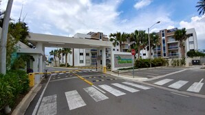 A gated entrance to a modern building with a pedestrian crossing and palm trees. - Tropical Condo BBQ Pool 5min to Airport (Puñal)