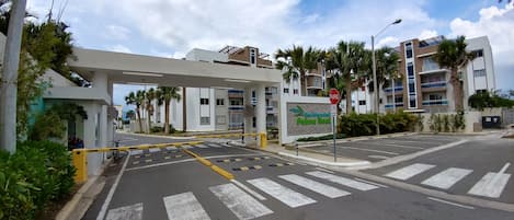 A gated entrance to a modern building with a pedestrian crossing and palm trees.