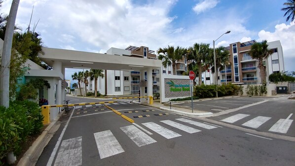 A gated entrance to a modern building with a pedestrian crossing and palm trees.