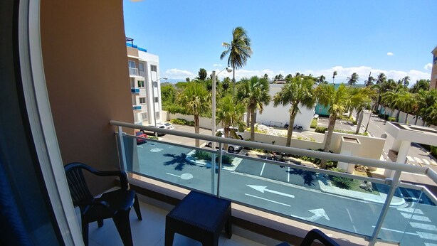 A balcony with a view of a parking lot, palm trees, and buildings. - Tropical Condo BBQ Pool 5min to Airport (Puñal)