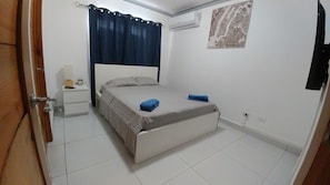 A bedroom with a bed, a nightstand, a wall-mounted air conditioner, and a map on the wall.