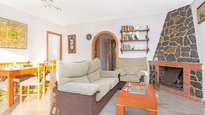 Una sala de estar acogedora con sofá, mesa de centro, chimenea, estantería y comedor.