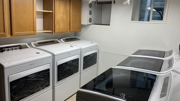 Une buanderie équipée d’une machine à laver et d’un sèche-linge superposés, de meubles en bois et d’une fenêtre.