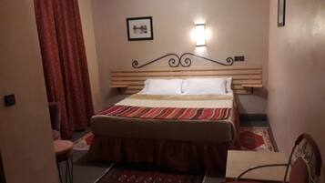 A bedroom with a bed, a chair, a small table, and a wall-mounted light fixture.