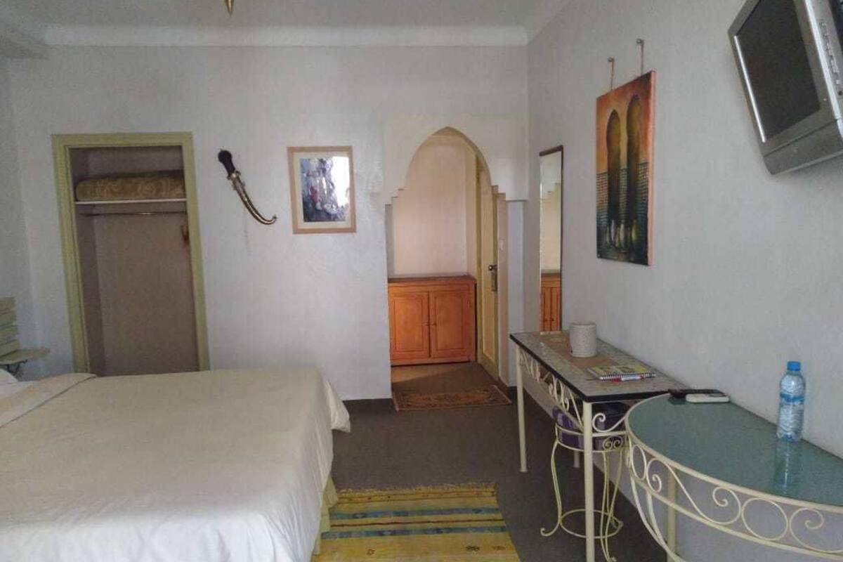 A hotel room with a bed, a desk with a chair, a television, and a bathroom visible through an archway.