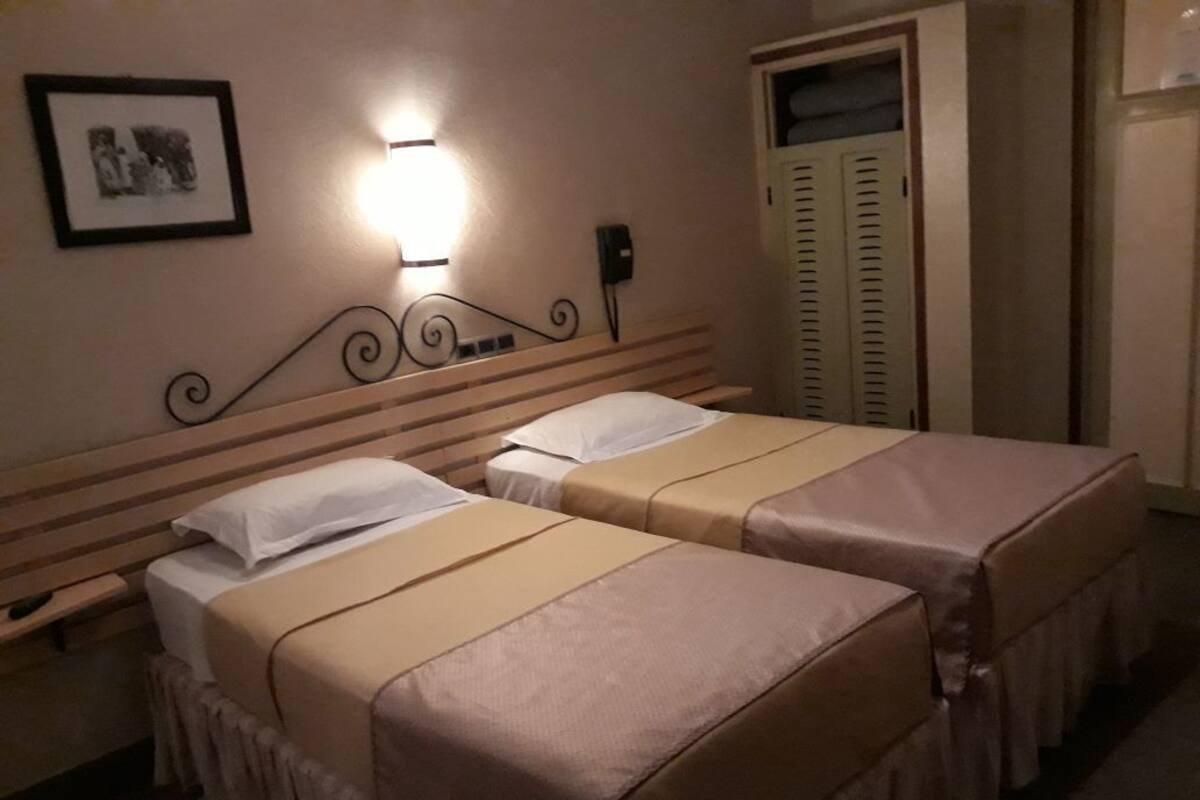 A hotel room with two beds, a bedside table, a wall-mounted light, a framed picture, and a closet with sliding doors.