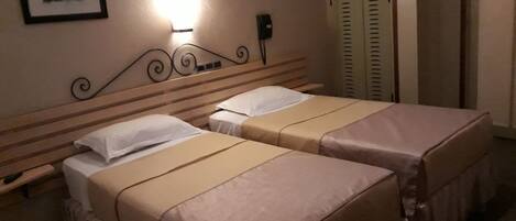 Habitación de hotel con dos camas, una mesita de noche, una lámpara de pared, un cuadro enmarcado y un armario con puertas correderas.
