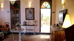 A cozy room with a traditional design, featuring a wooden cabinet, a television, a table with a vase of flowers, and a framed picture on the wall. - Hotel Royal (Oujda)