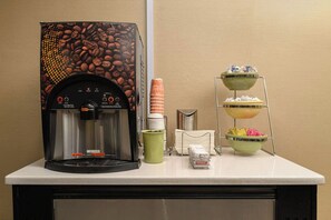 Una cafetera, vasos desechables, un dispensador de condimentos y un atril de tres niveles para salsas en una encimera.