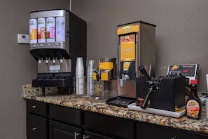 A coffee station with a coffee machine, syrup dispenser, waffle maker, and a bottle of sugar-free syrup. - Quality Inn Lexington (Lexington)