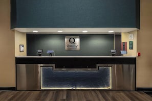 A hotel reception desk with a 'Quality by Choice Hotels' sign, a digital check-in kiosk, and a welcome sign. - Quality Inn Lexington (Lexington)