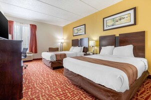 Habitación de hotel con dos camas, un escritorio, una silla, un televisor y una ventana con cortinas.
