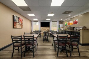 Un comedor con varias mesas y sillas, una zona de cocina con alimentos a la vista, y una pared de piedra.